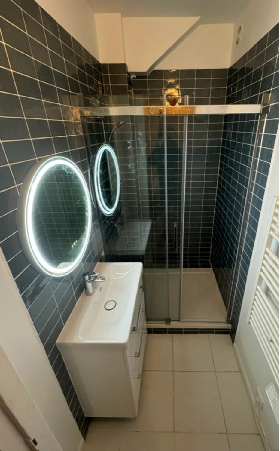 Après rénovation : douche vitrée, carrelage bleu et meuble vasque avec miroir lumineux