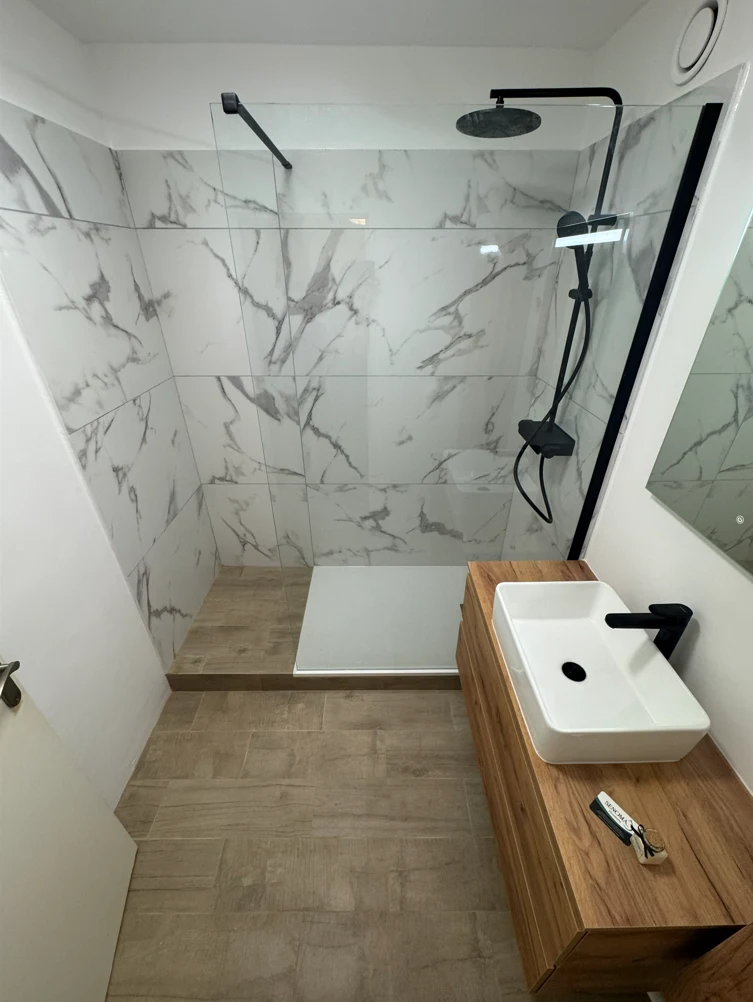 Après rénovation : douche ouverte, carrelage effet marbre, meuble en bois et robinetterie noire