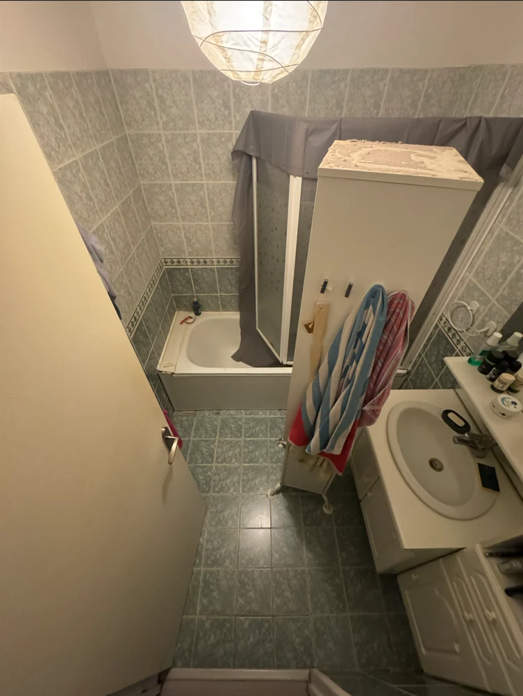 Avant rénovation : douche fermée, carrelage gris et meuble lavabo blanc