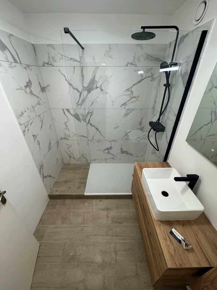 Salle de bain avec douche vitrée, carrelage effet marbre et meuble vasque en bois