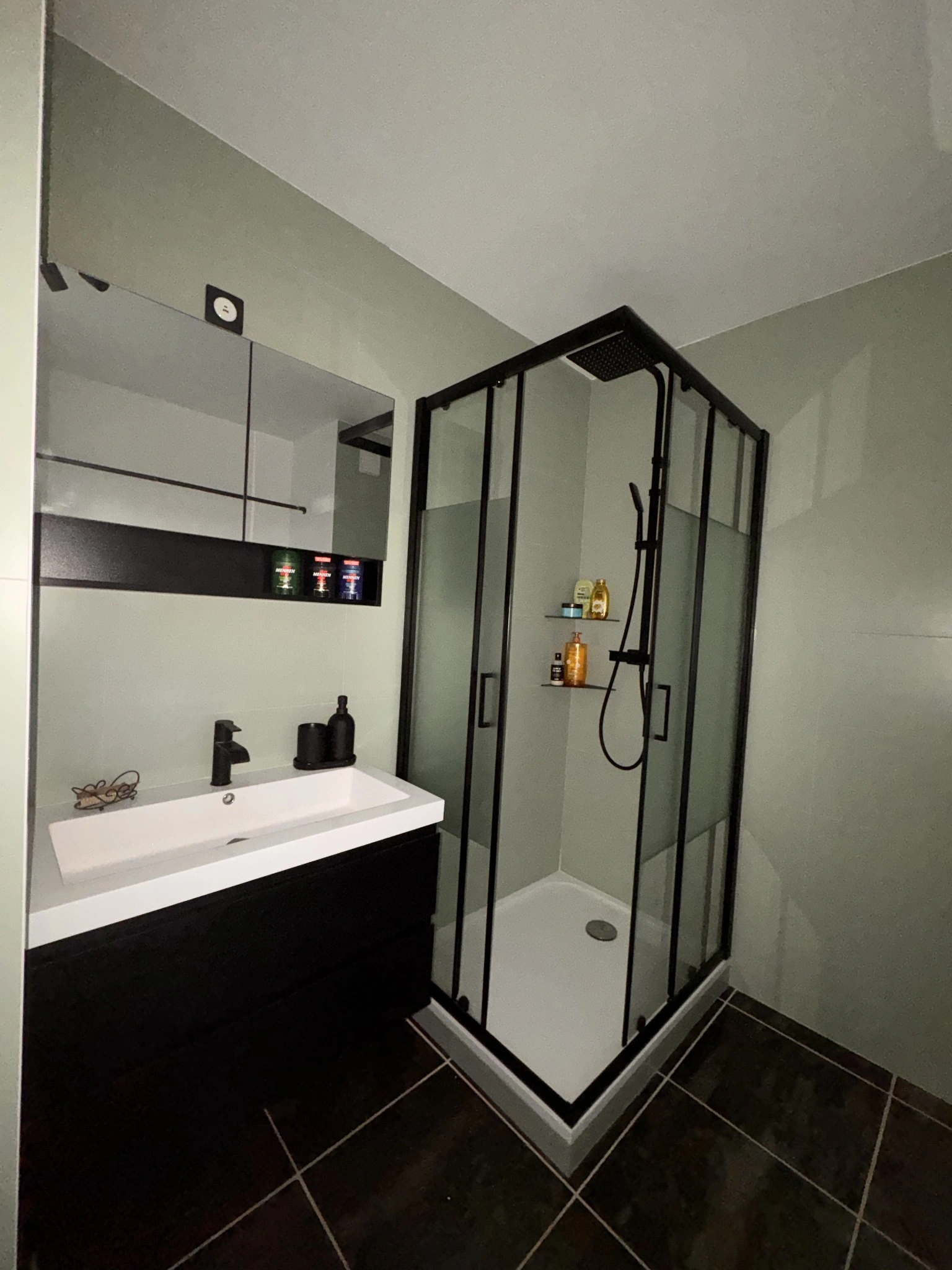 Salle de bain avec douche vitrée à profils noirs, vasque blanche, meuble noir et carrelage vert clair